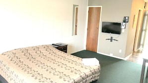 Una habitación de hotel con una cama, una mesita de noche, un televisor montado en la pared y una puerta.
