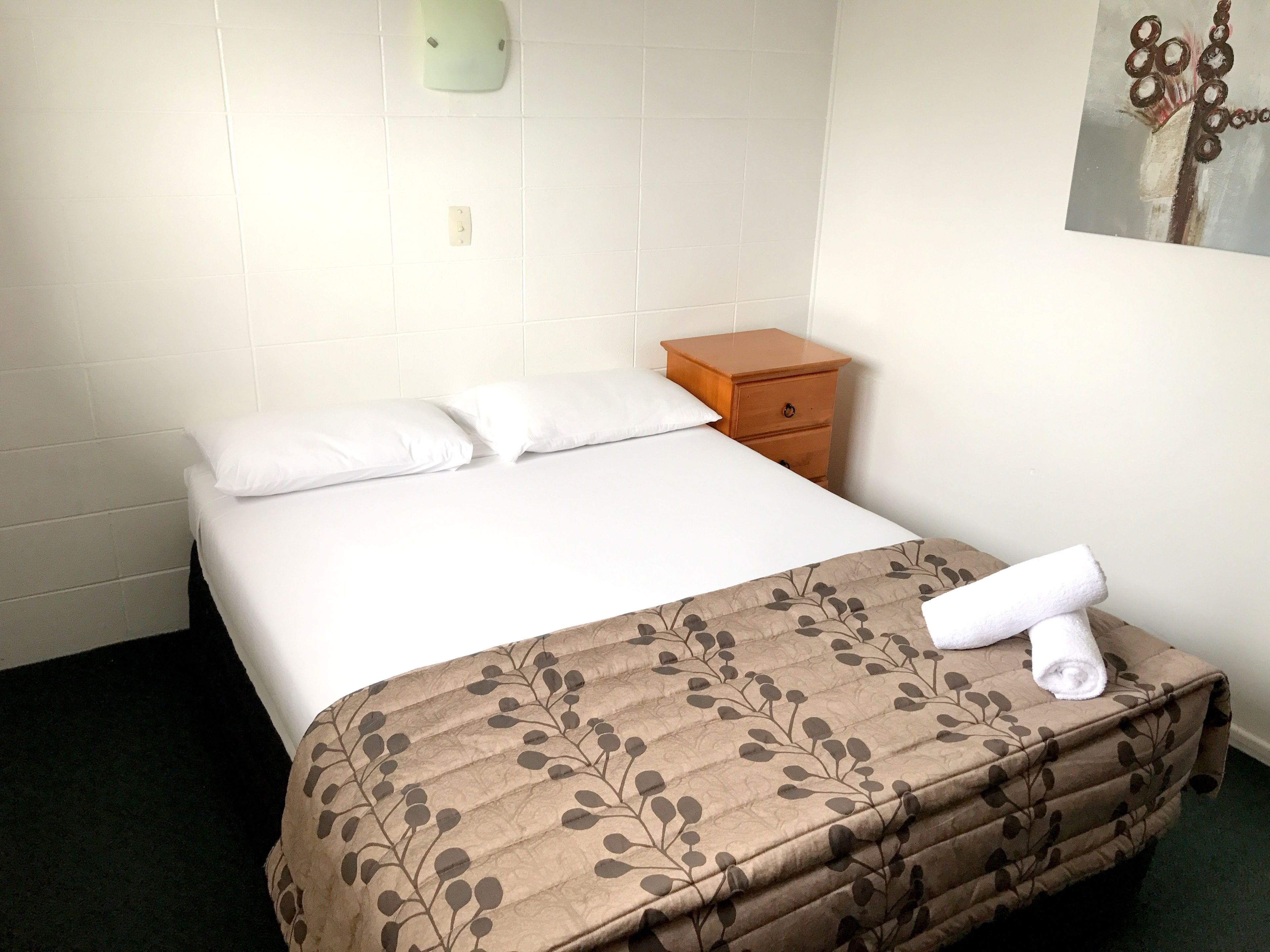 A hotel room with a bed, a wooden nightstand, and a wall-mounted light fixture.