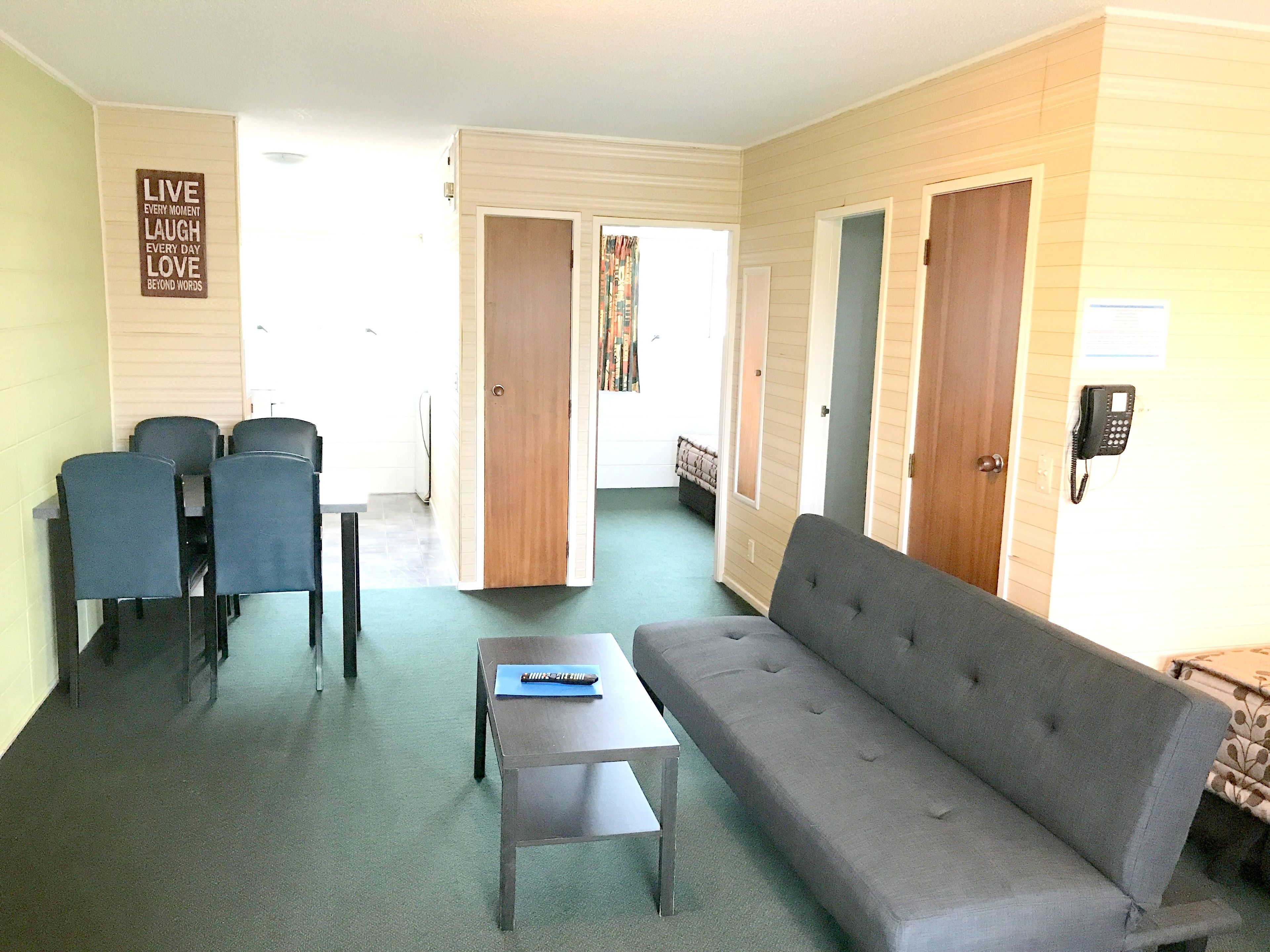 A living room with a sofa, a coffee table, and two chairs. There is a dining table with chairs, a door, and a telephone.