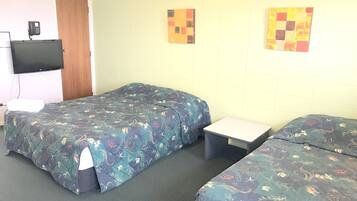 A hotel room with two beds, a small table, a TV mounted on the wall, and artwork on the wall.
