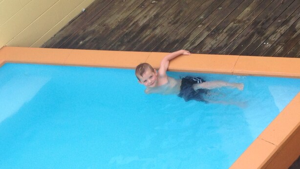 Niño en una piscina con un muelle de madera alrededor.