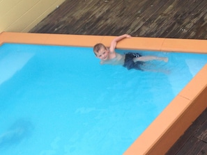 Un enfant dans une piscine, entourée d’une terrasse en bois.