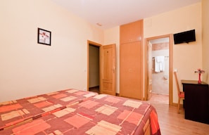 Un dormitorio con cama, armario, televisión y baño visible a través de una puerta abierta.