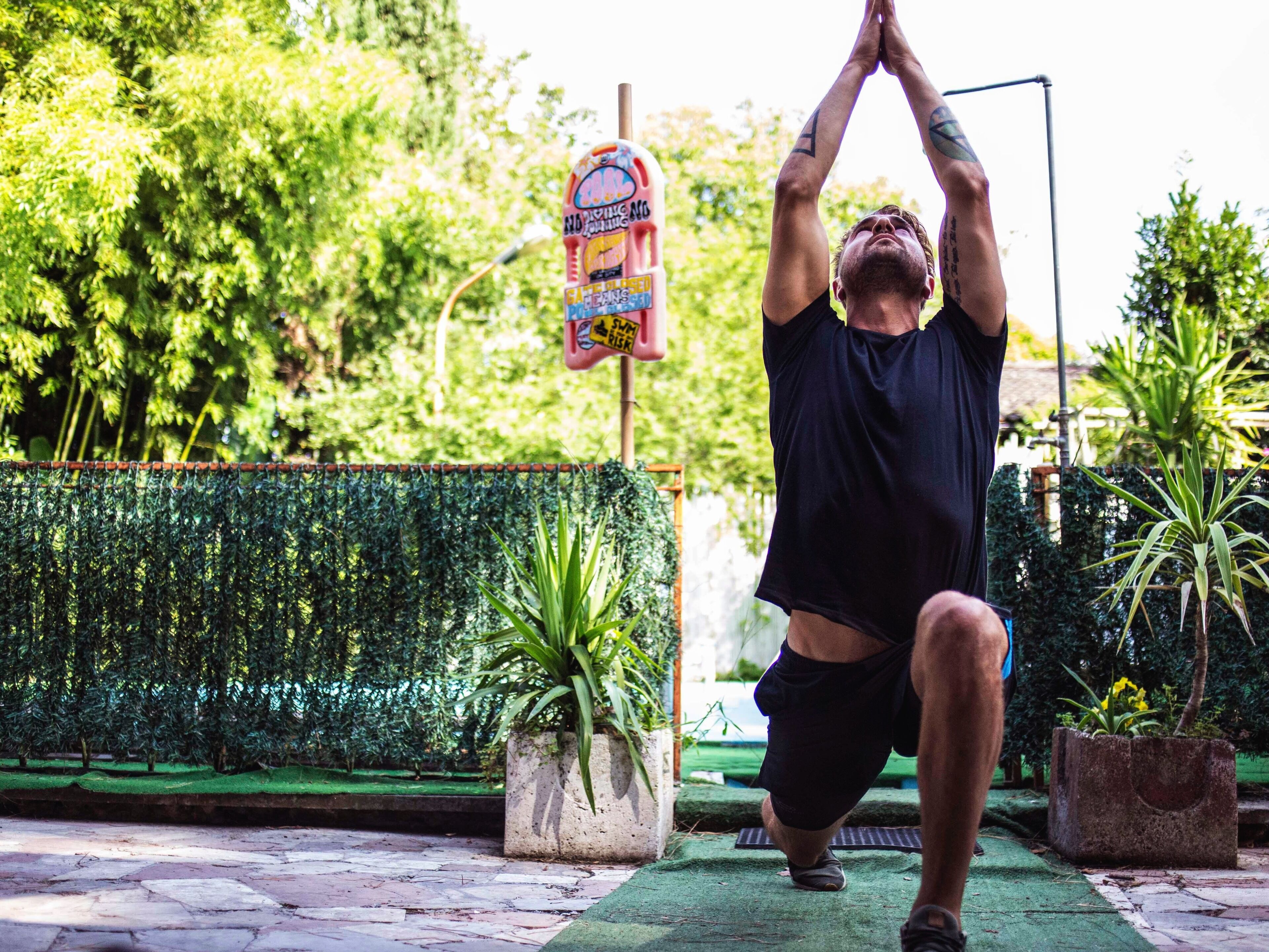 Una persona realizando una postura de yoga al aire libre, con follaje y un cartel de fondo.