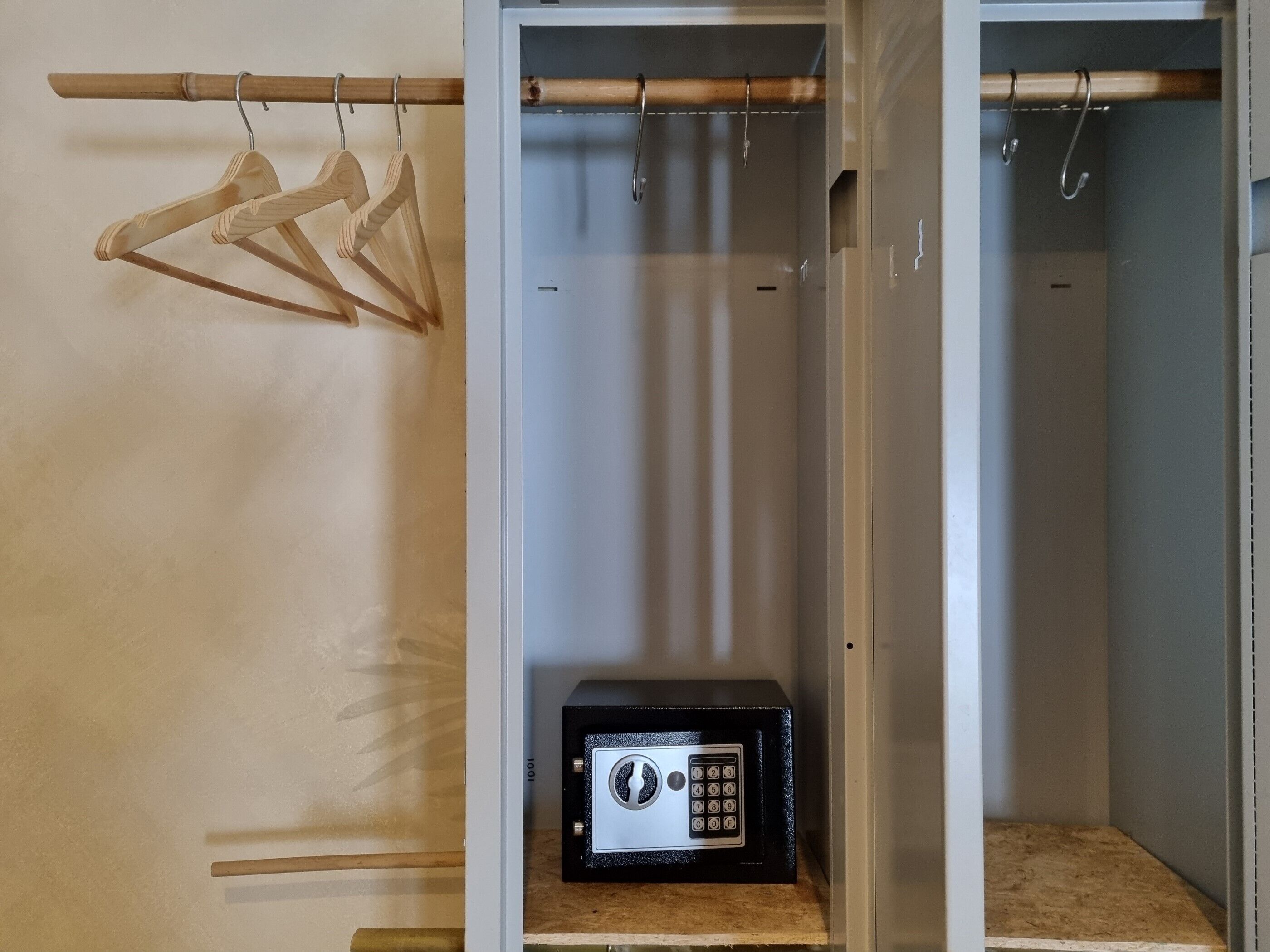 A walk-in closet with a wooden hanger rack, a black safe, and a mirror.