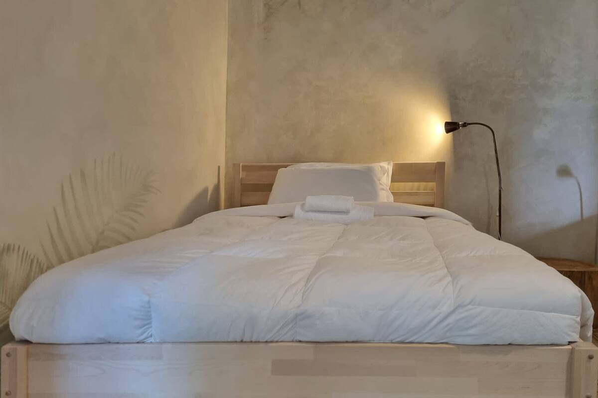A neatly made bed with white bedding and a wooden headboard.