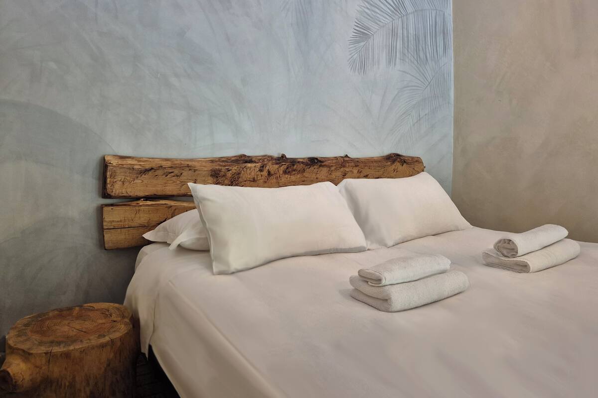 A bed with white linens, two pillows, and folded towels.