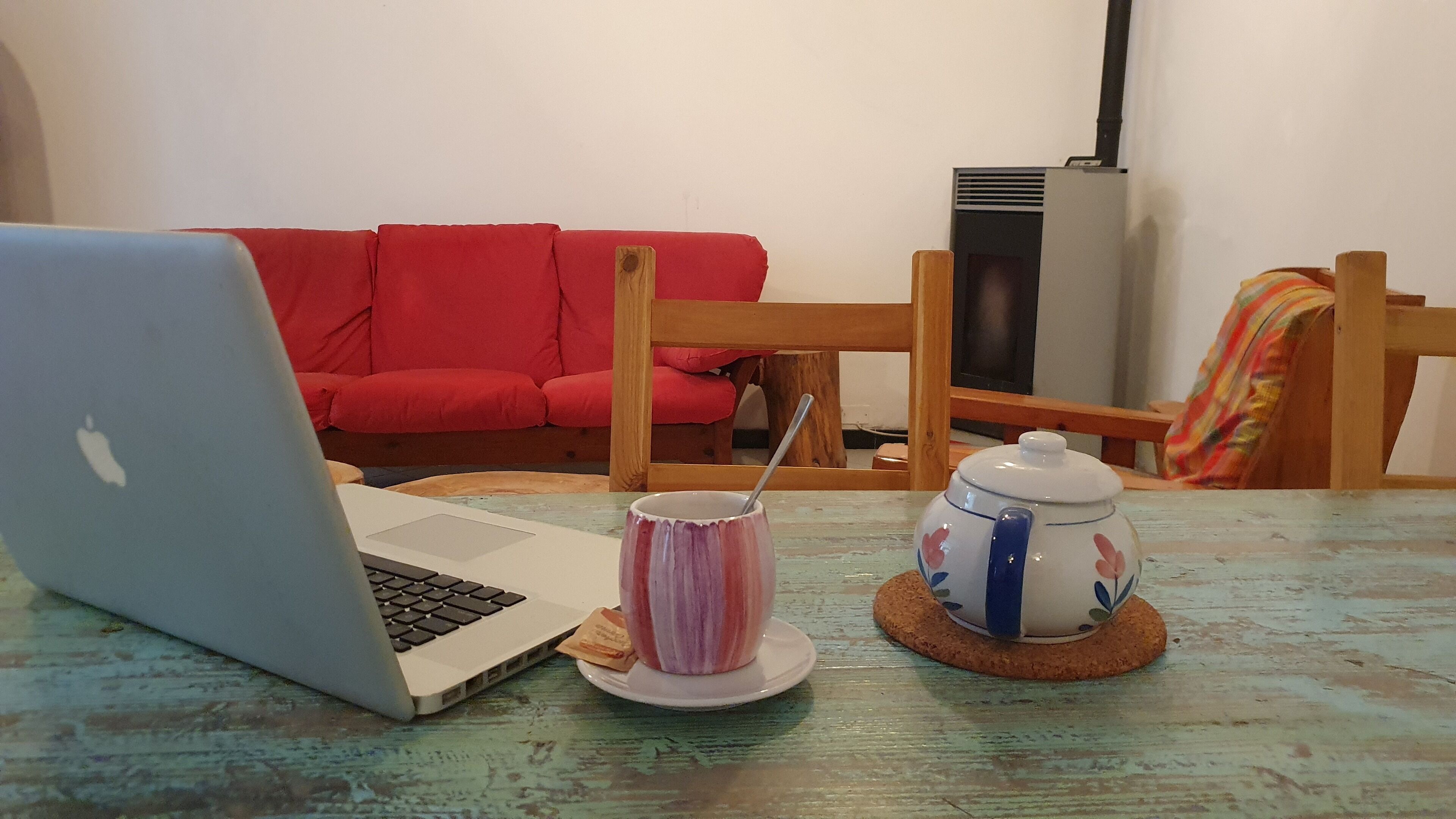 Una laptop sobre una mesa con una taza y una tetera.