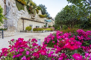 Un edificio de piedra con tejado de baldosas, rodeado de vibrantes flores rosadas y exuberante follaje.