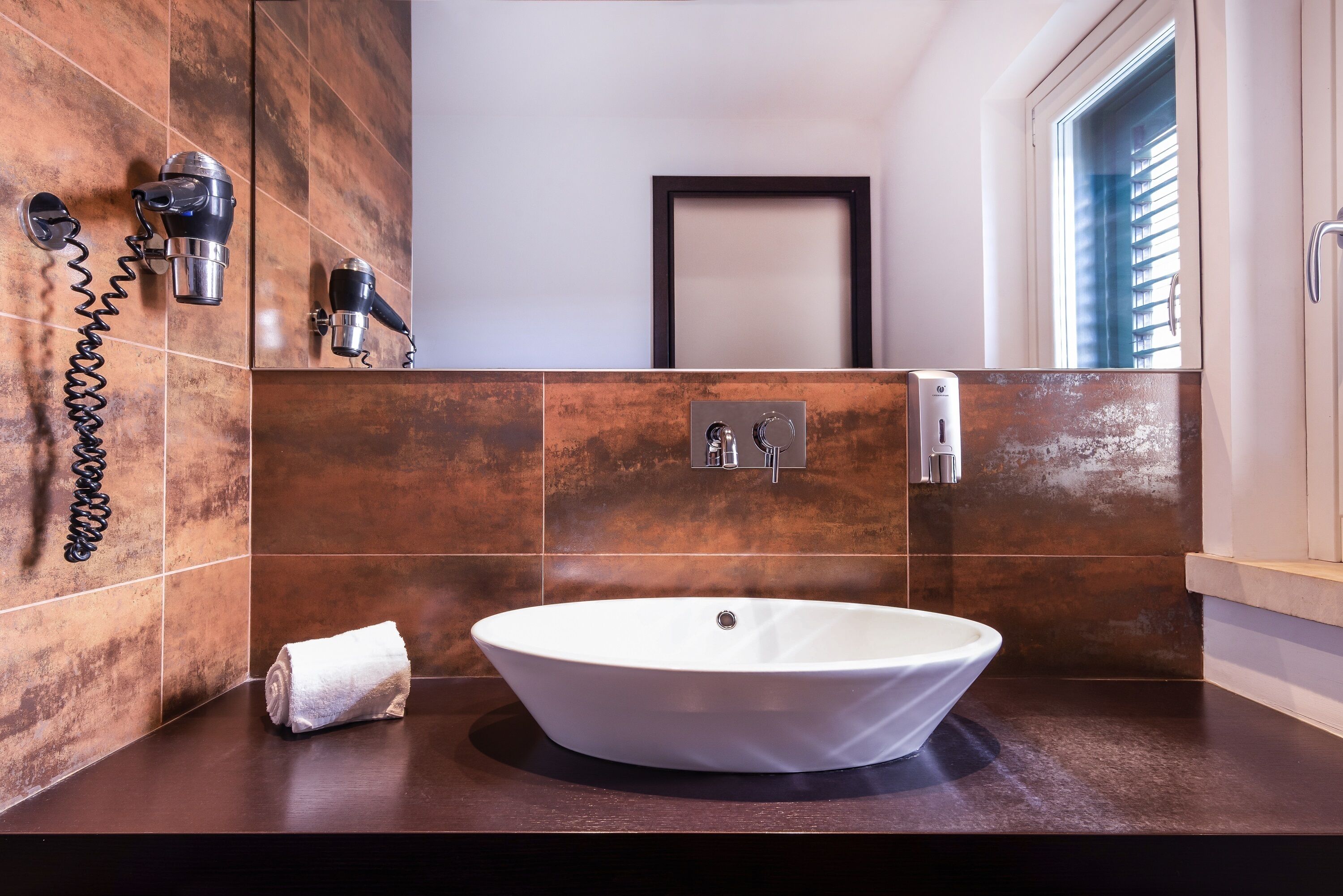 A bathroom with a large oval sink, a towel, and two hair dryers mounted on the wall.