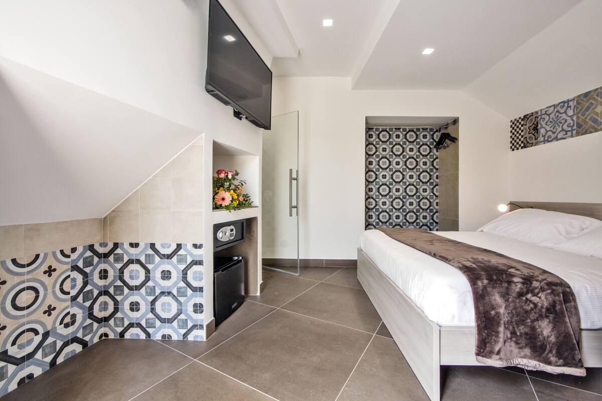 Une chambre d’hôtel moderne équipée d’un lit, d’un téléviseur fixé au mur, d’une petite kitchenette et de carreaux décoratifs sur les murs.
