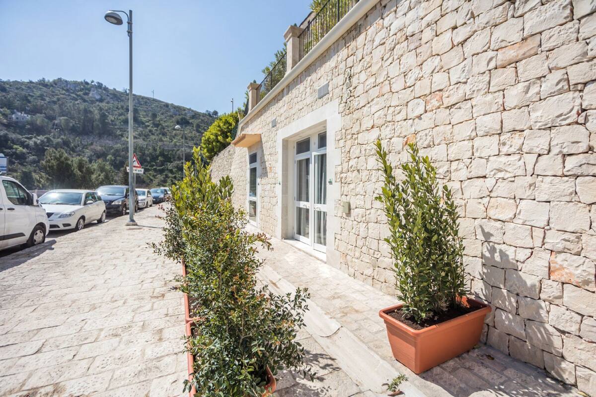 Un bâtiment en pierre avec une allée pavée, des voitures garées et des plantes en pot.