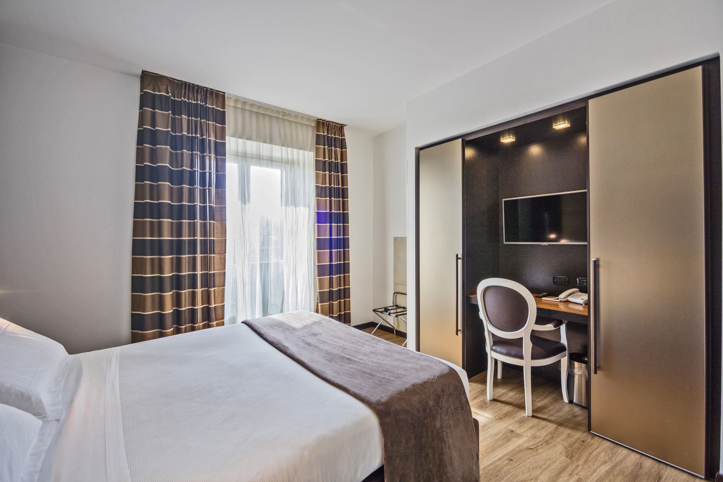 Una habitación de hotel con cama, escritorio con silla, televisor y armario.
