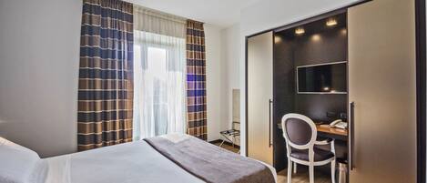 Una habitación de hotel con cama, escritorio con silla, televisor y armario.