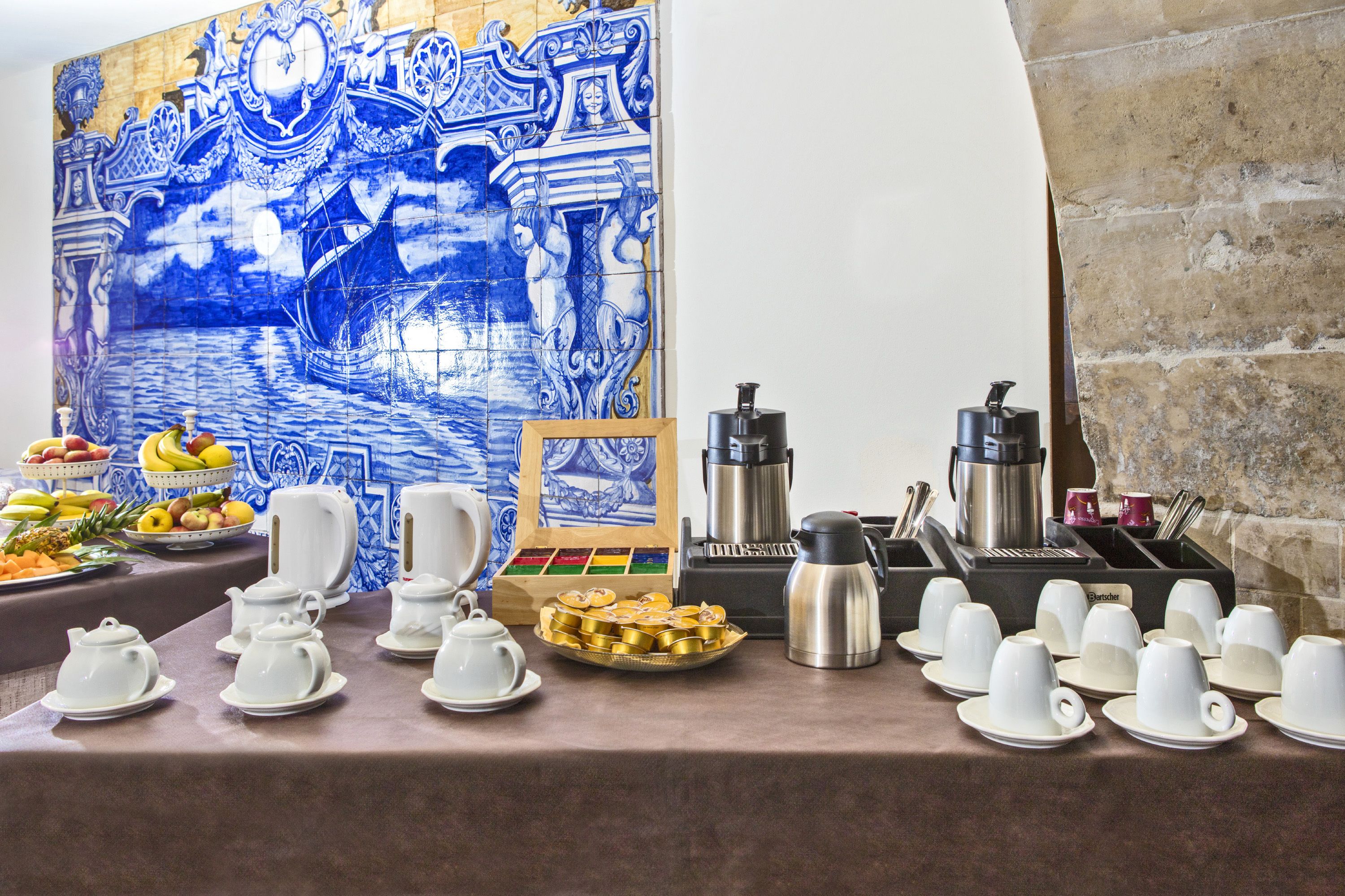 A breakfast buffet setup with various food items, tea and coffee stations, and a decorative blue tile wall.