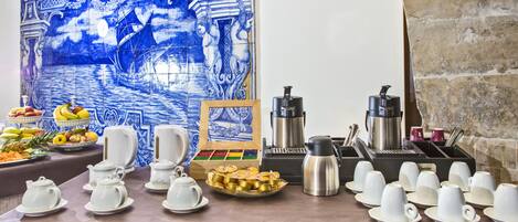 A breakfast buffet setup with various food items, tea and coffee stations, and a decorative blue tile wall.