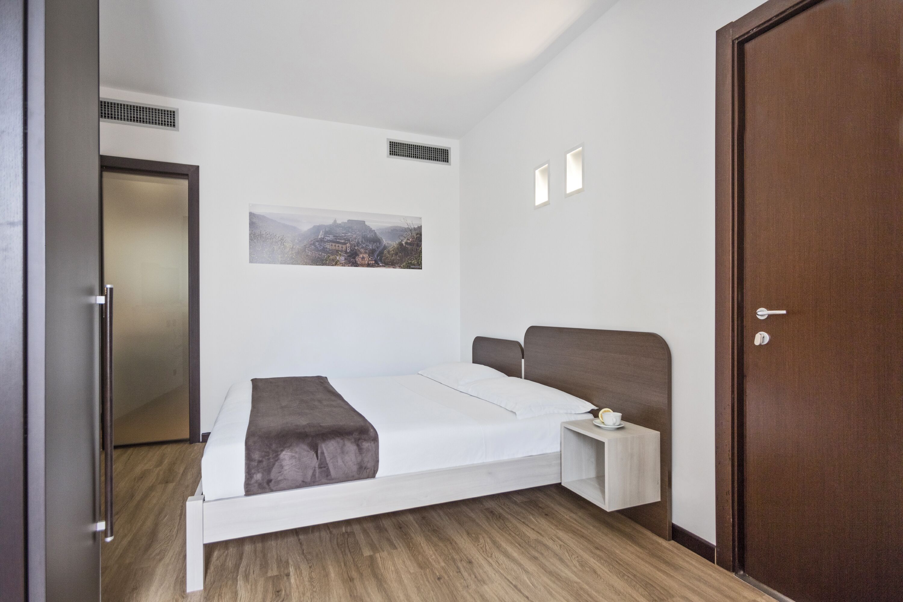 Un dormitorio moderno con cama, mesita de noche, un cuadro en la pared y una puerta.