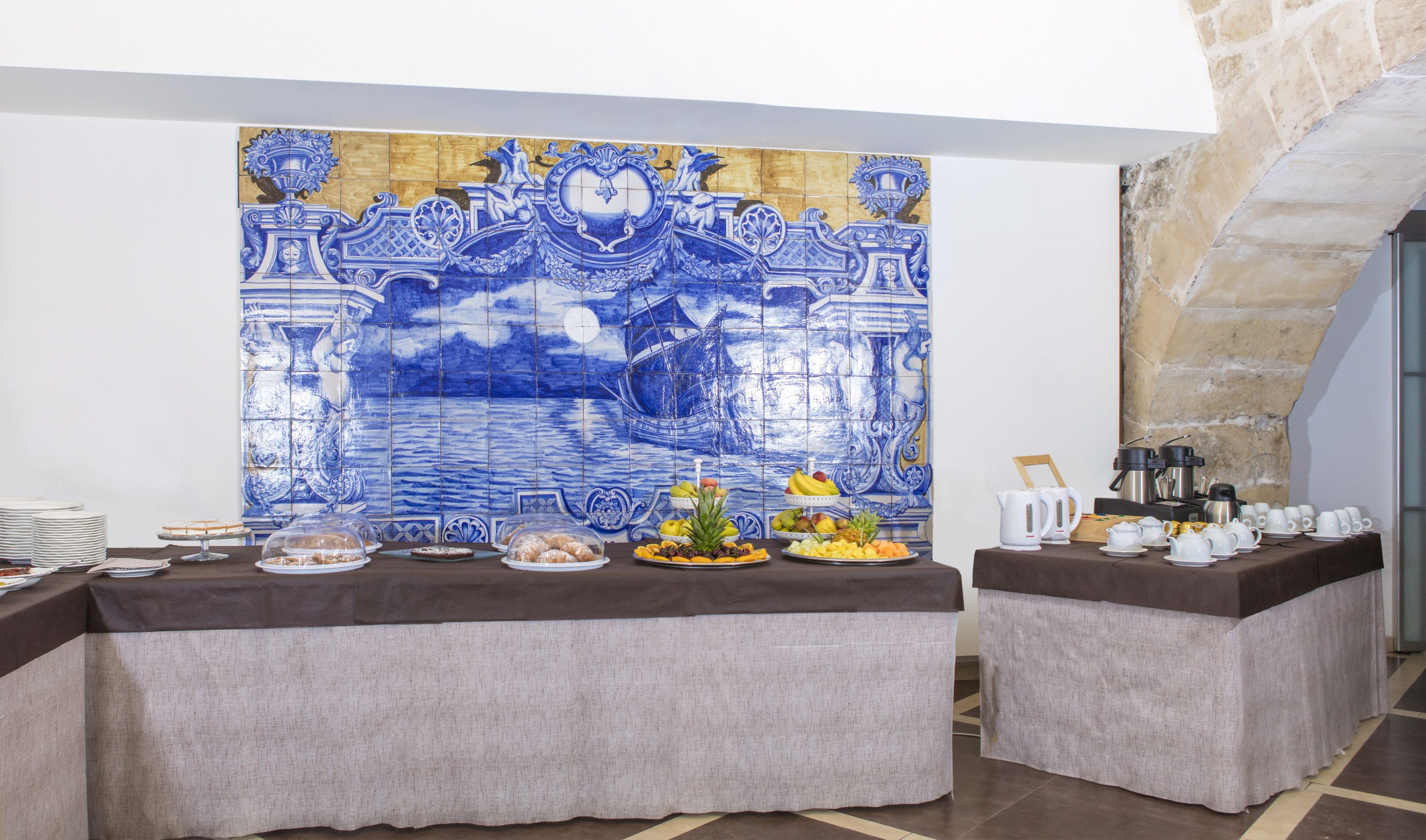 Un buffet disposé devant un décor composé de carreaux bleus et dorés, avec deux comptoirs de service et une grande variété de plats et de boissons.