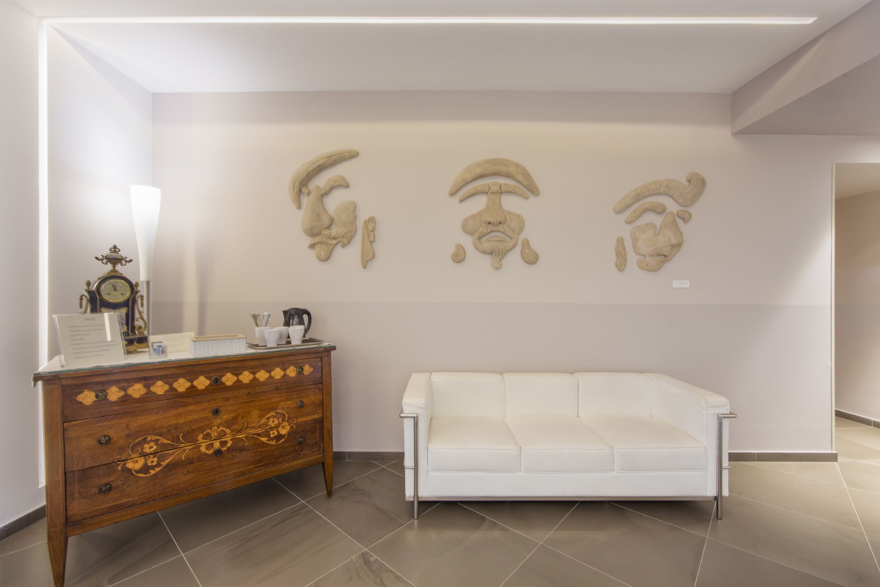 A modern room with a white sofa, a wooden dresser with decorative carvings, and wall-mounted sculptures.