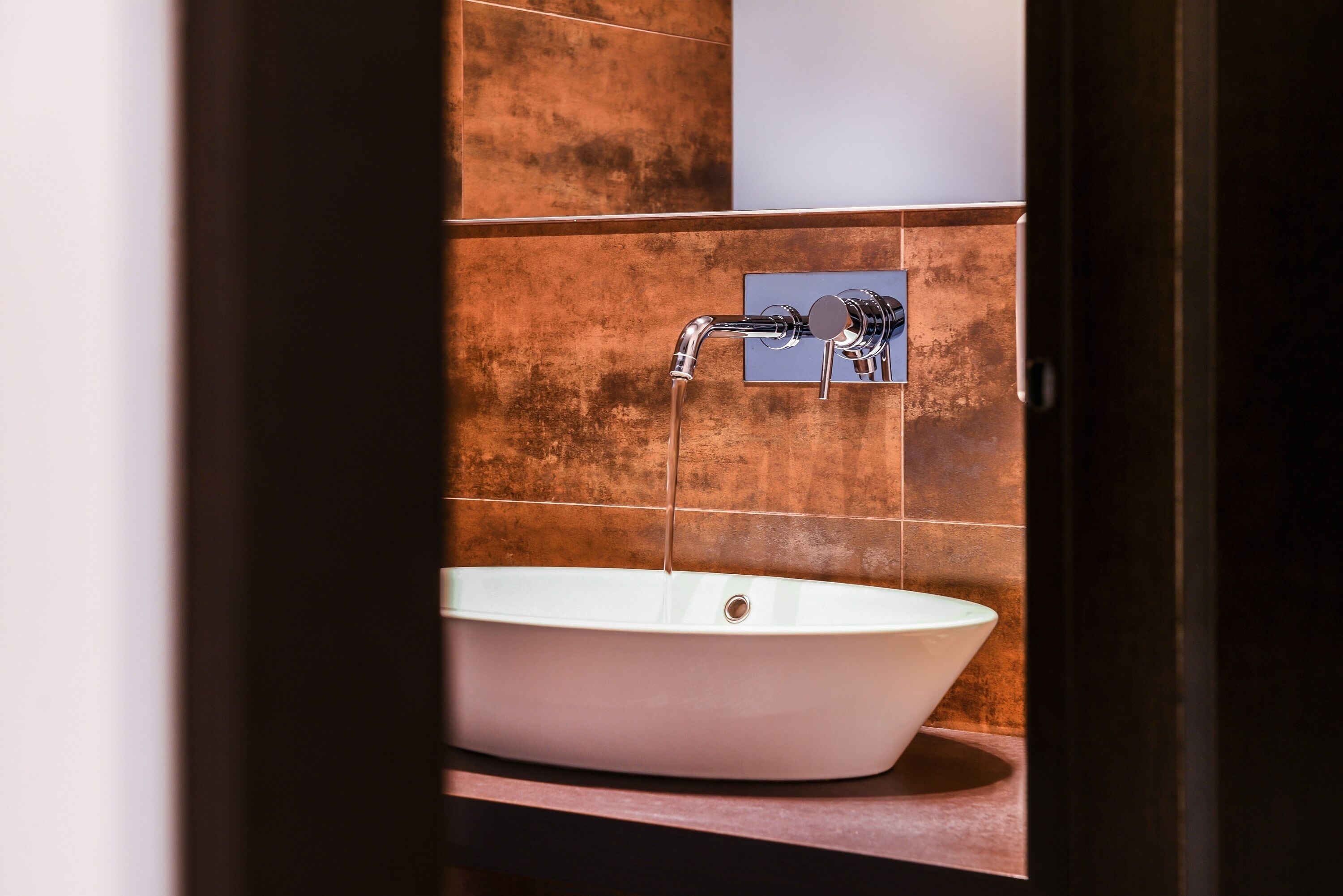 Un baño con un lavamanos blanco, un grifo cromado y paredes de azulejos marrones.