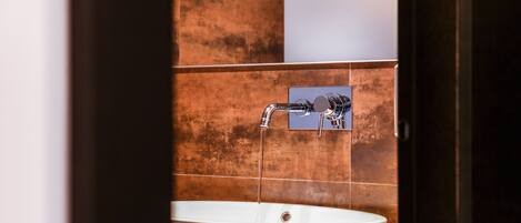 Un baño con un lavamanos blanco, un grifo cromado y paredes de azulejos marrones.