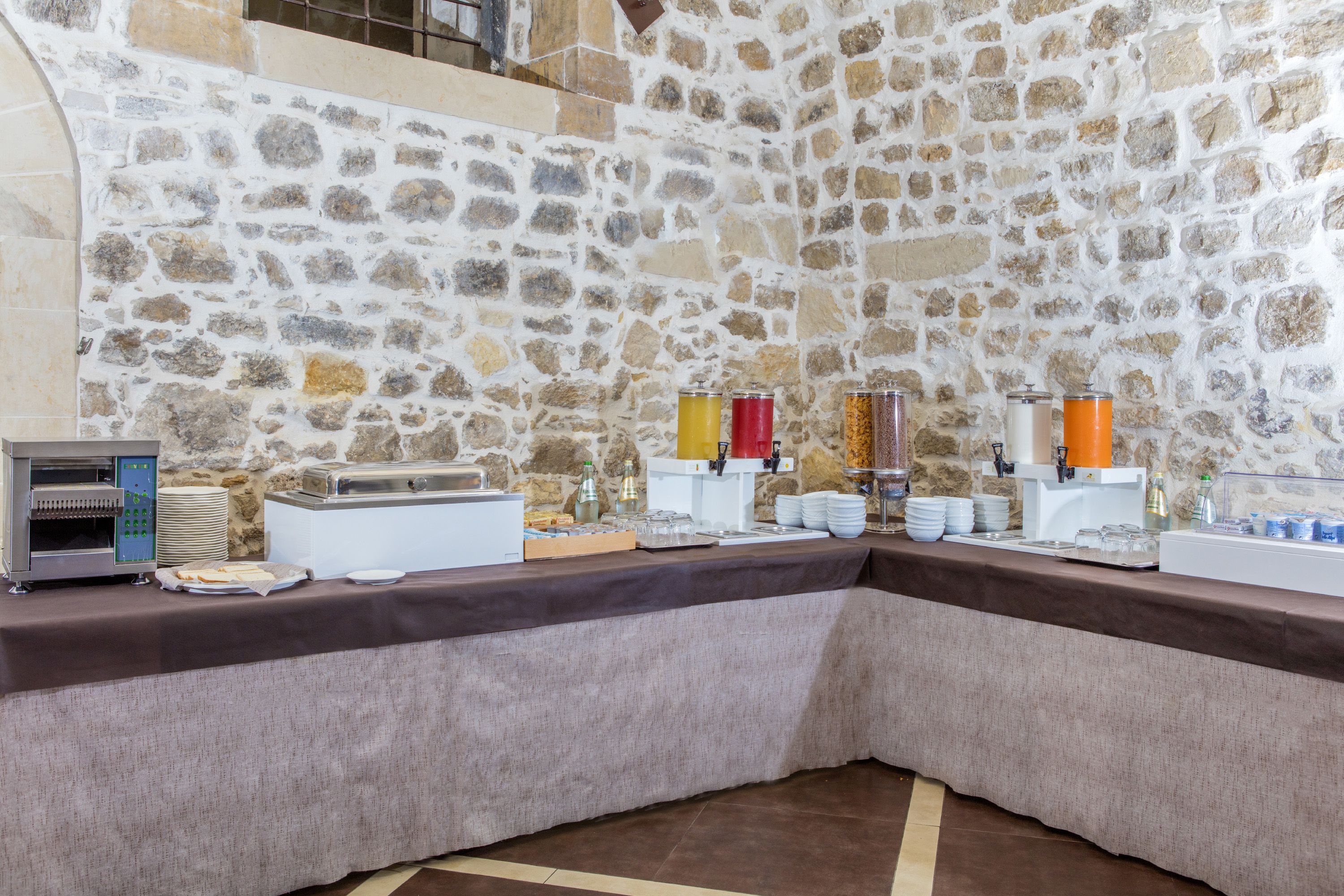 Ein Buffet mit Stehwand im Hintergrund, einer Selbstbedienungsgetränkestation und verschiedenen Speisen auf einem Tisch.