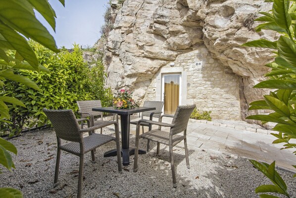 Un área de estar al aire libre con sillas de mimbre y una mesa, frente a una pared de piedra con una puerta.