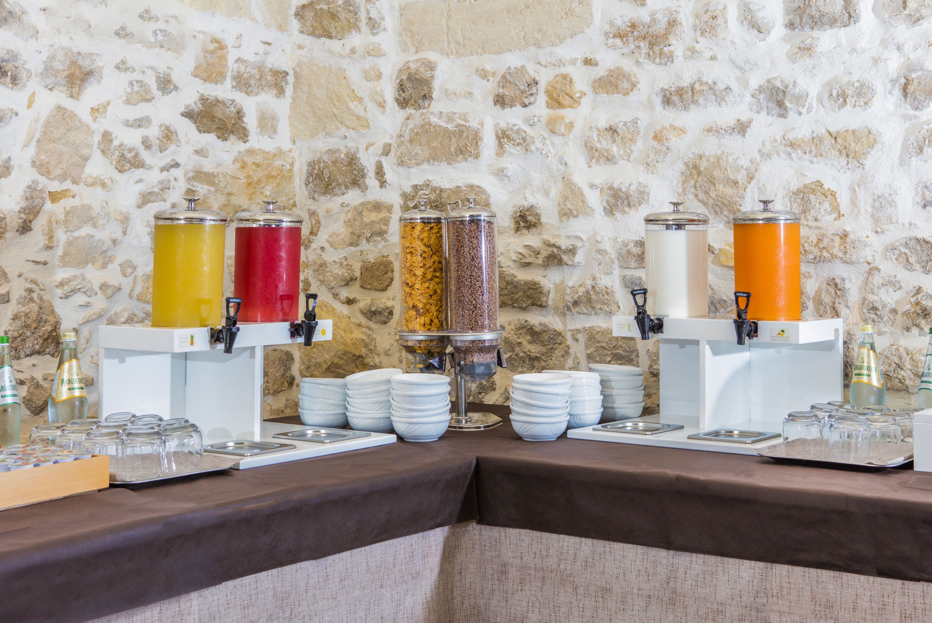 A buffet setup with various food dispensers and serving dishes against a stone wall.