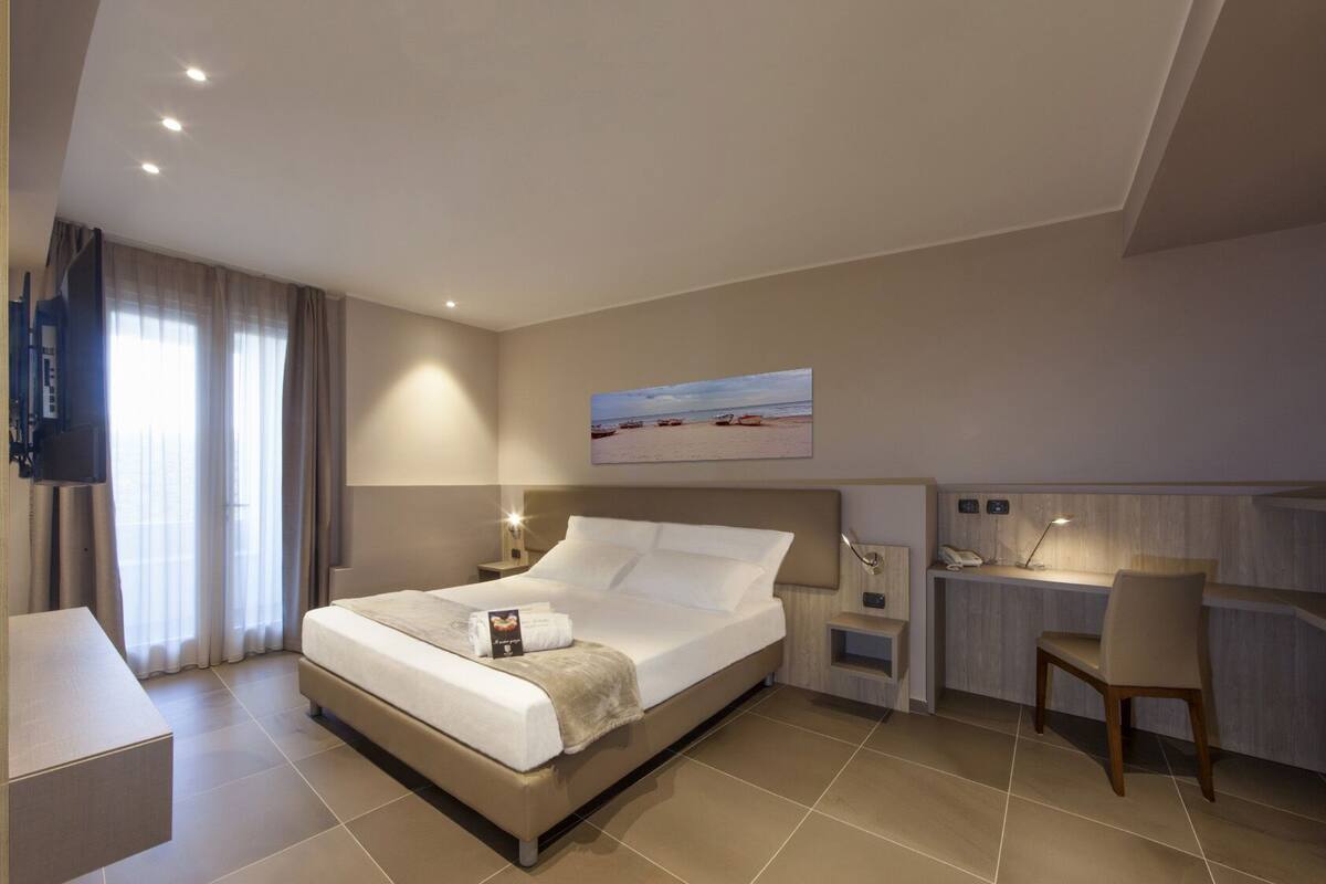 Une chambre d’hôtel avec un lit, un bureau, une chaise, une télévision et un tableau au mur.