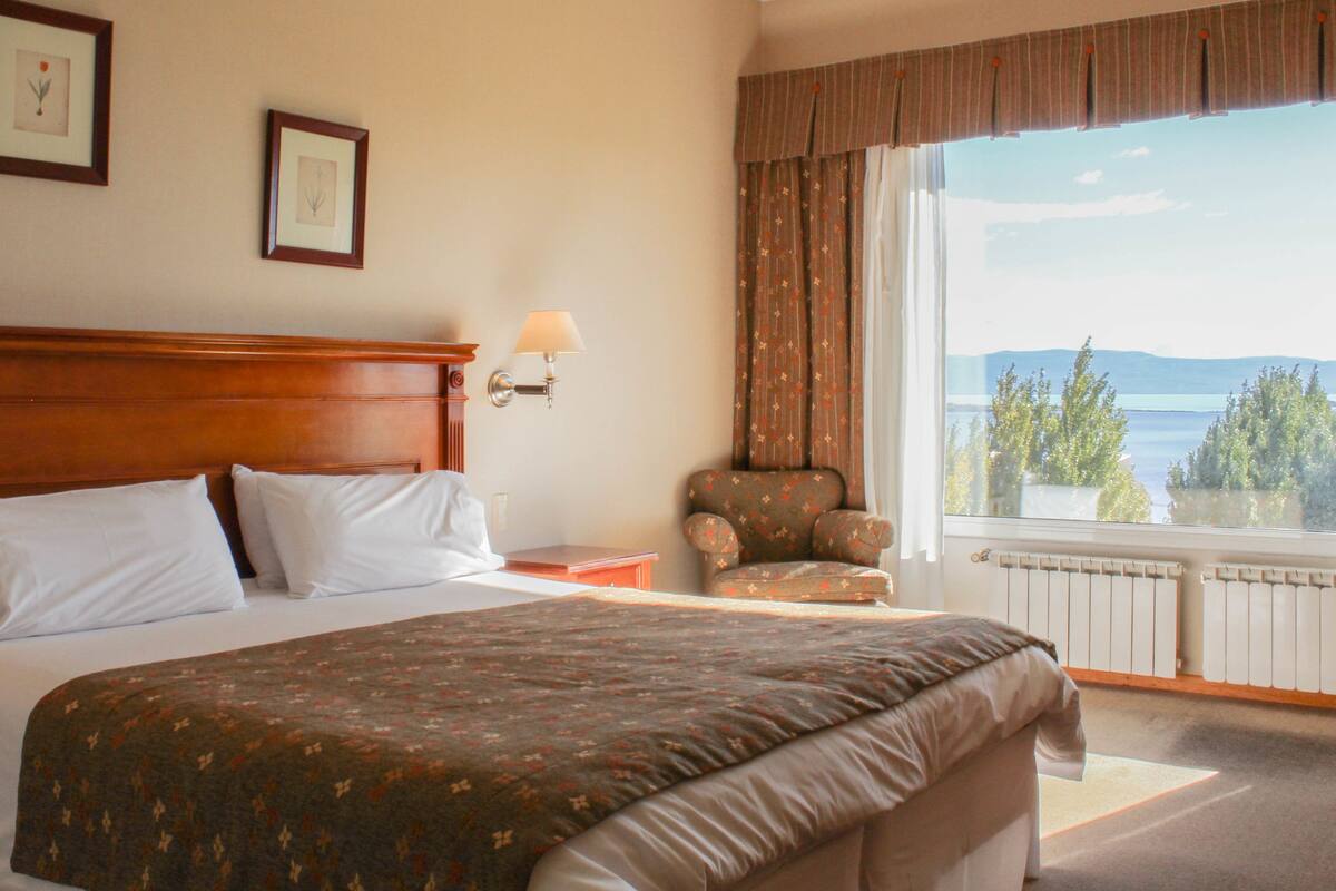 A hotel room with a large bed, a chair, a nightstand, and a window with a view of the outdoors.
