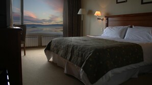 Camera d'albergo con un letto, una poltrona, una finestra vista mare e una lampada a parete.