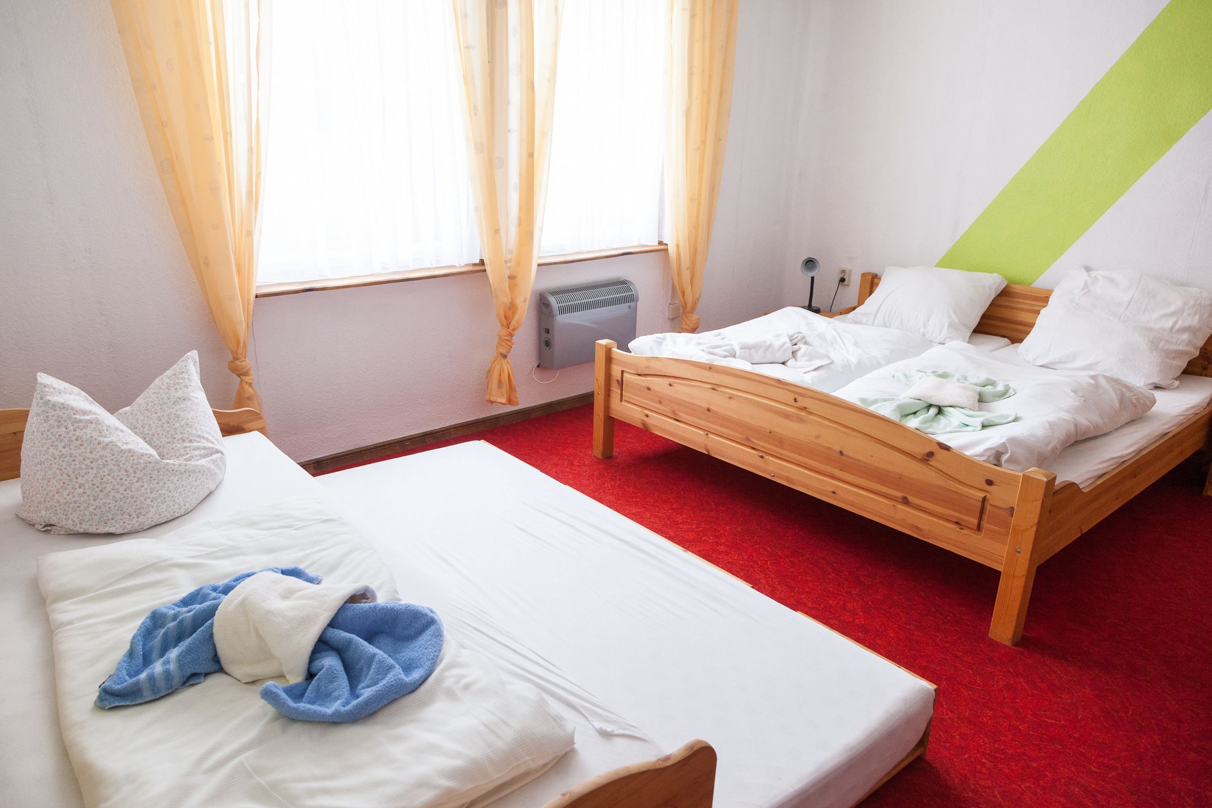 A room with two wooden beds, a red carpet, a window with curtains, and a green accent wall.