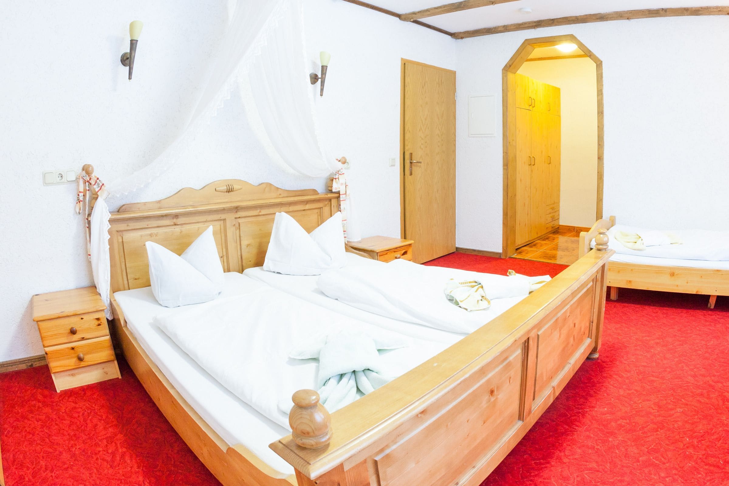 A wooden bed with white bedding, a wooden nightstand, a wooden wardrobe, and a mirror on the wall.
