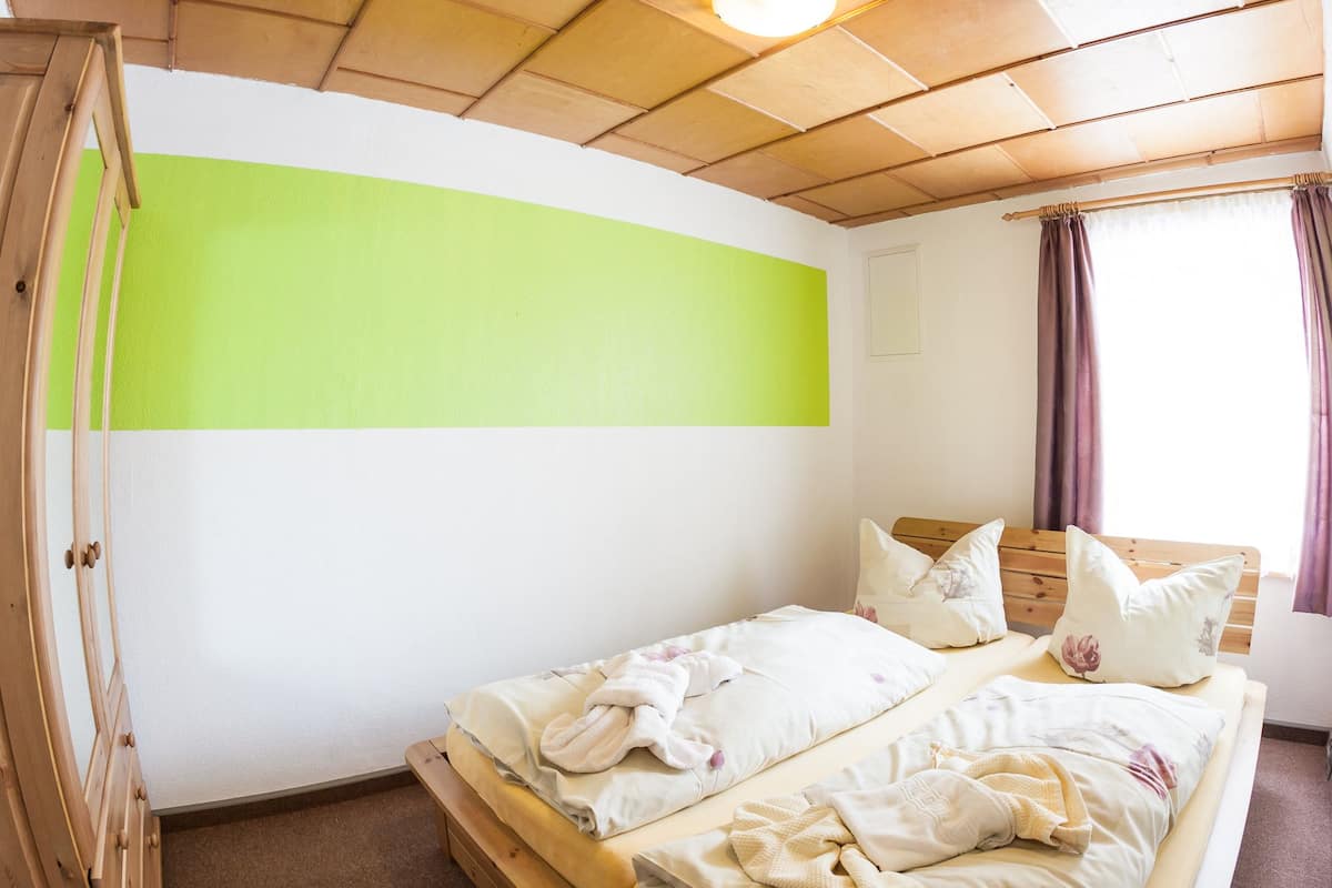 A room with a bed, a green wall, a wooden ceiling, and a window with curtains.
