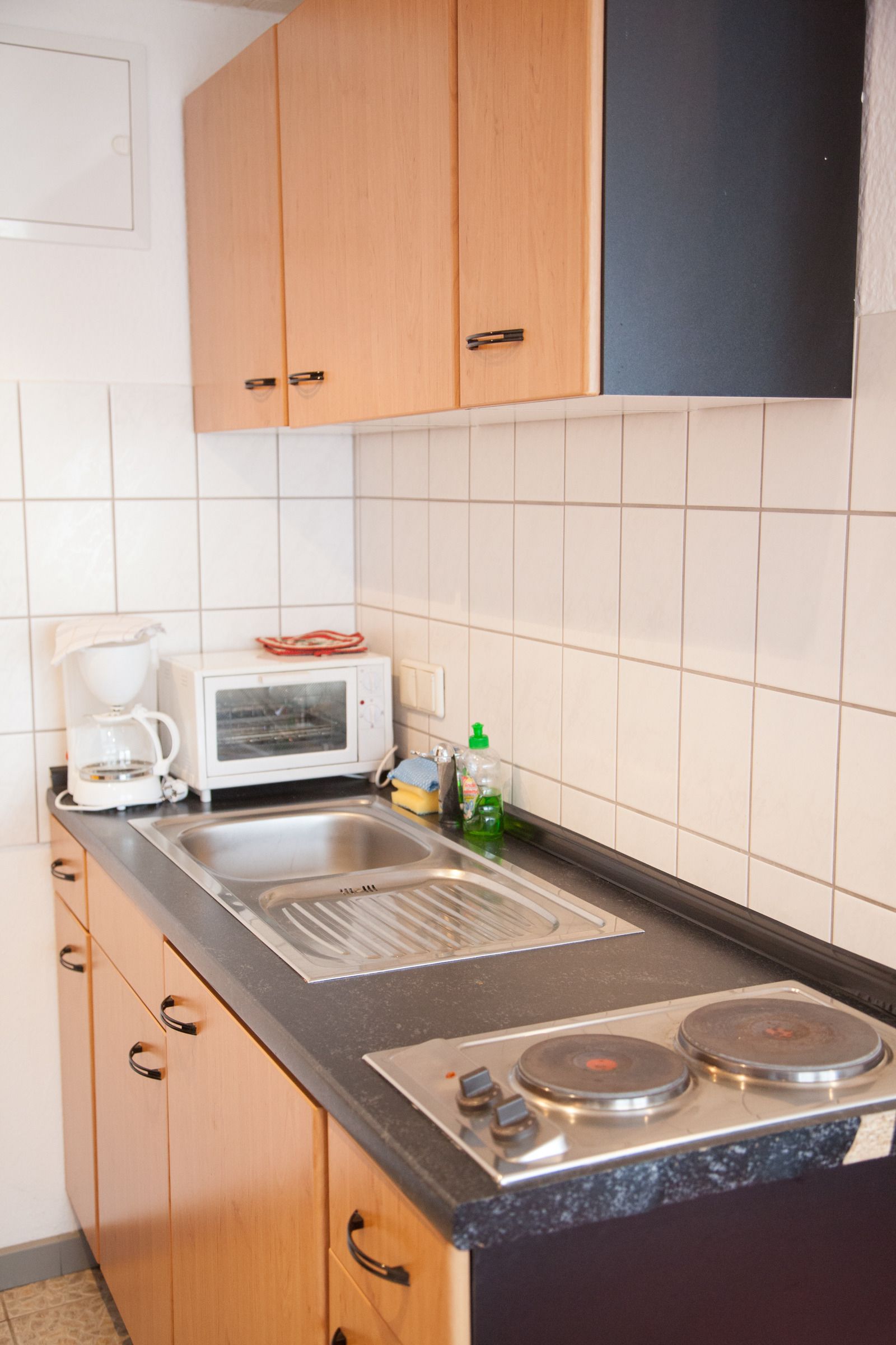 Una cocina compacta con armarios de madera, microondas, cafetera y fregadero.