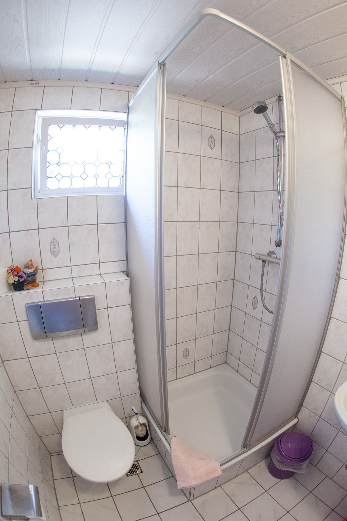 A small bathroom with a shower, toilet, and a window with a decorative grille.