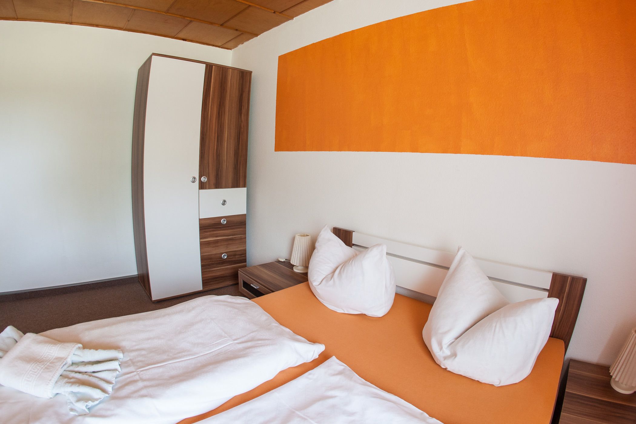A hotel room with a bed, a wardrobe, and a nightstand.