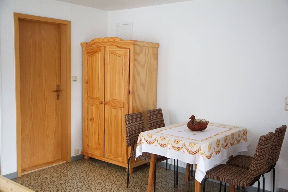 A dining area with a table set for two, a wooden cabinet, and patterned flooring.