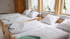 A room with two wooden beds, white bedding, a nightstand with a lamp, and a window with sheer curtains. - Pension Waldoase Hirschbüchenkopf (Harzgerode)