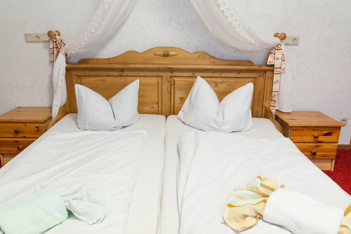 A double bed with white linens and two pillows, wooden nightstands, and a wooden headboard.