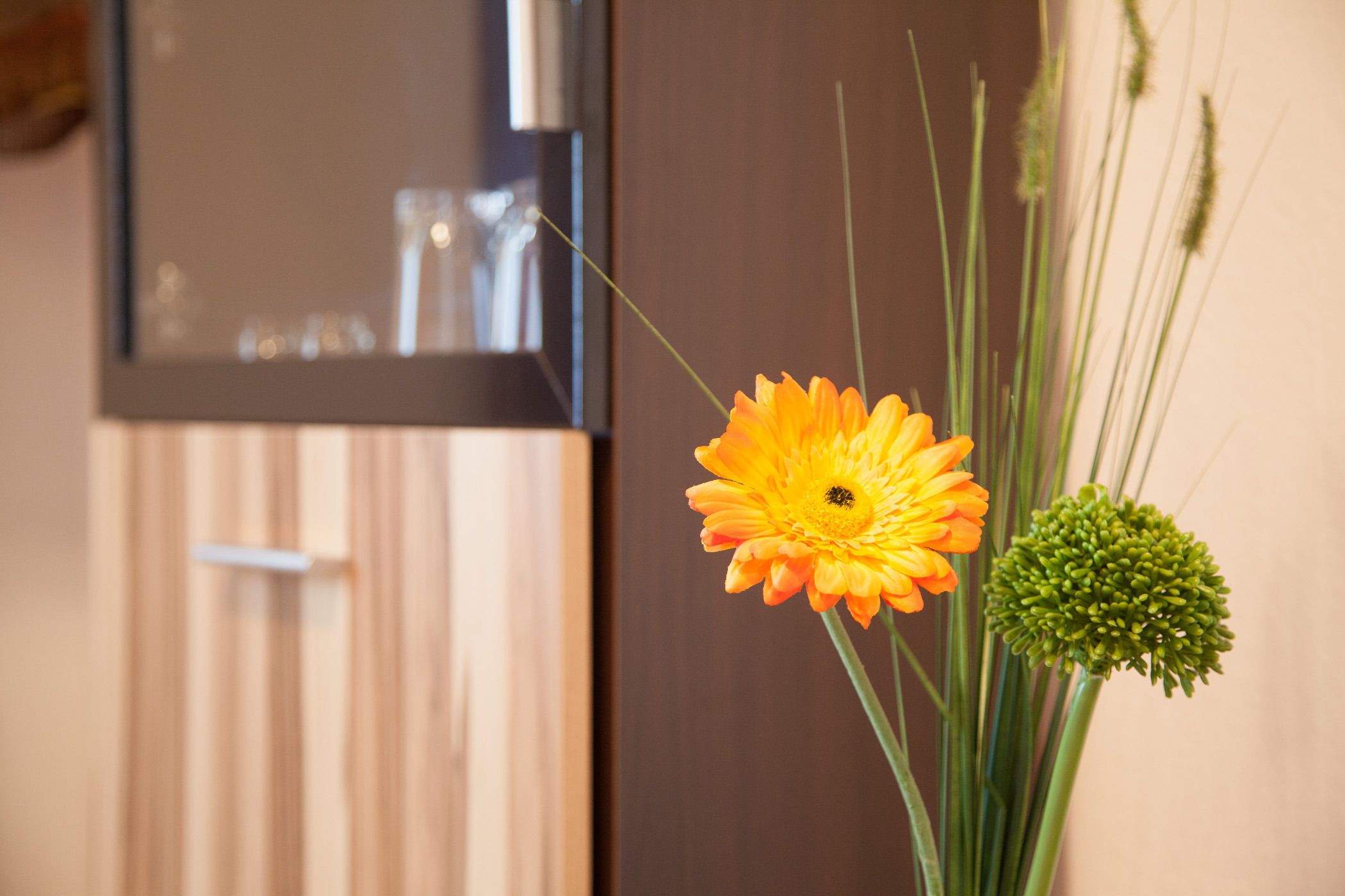 A room with a wooden floor, a mirror, and a vase with a flower and green foliage.