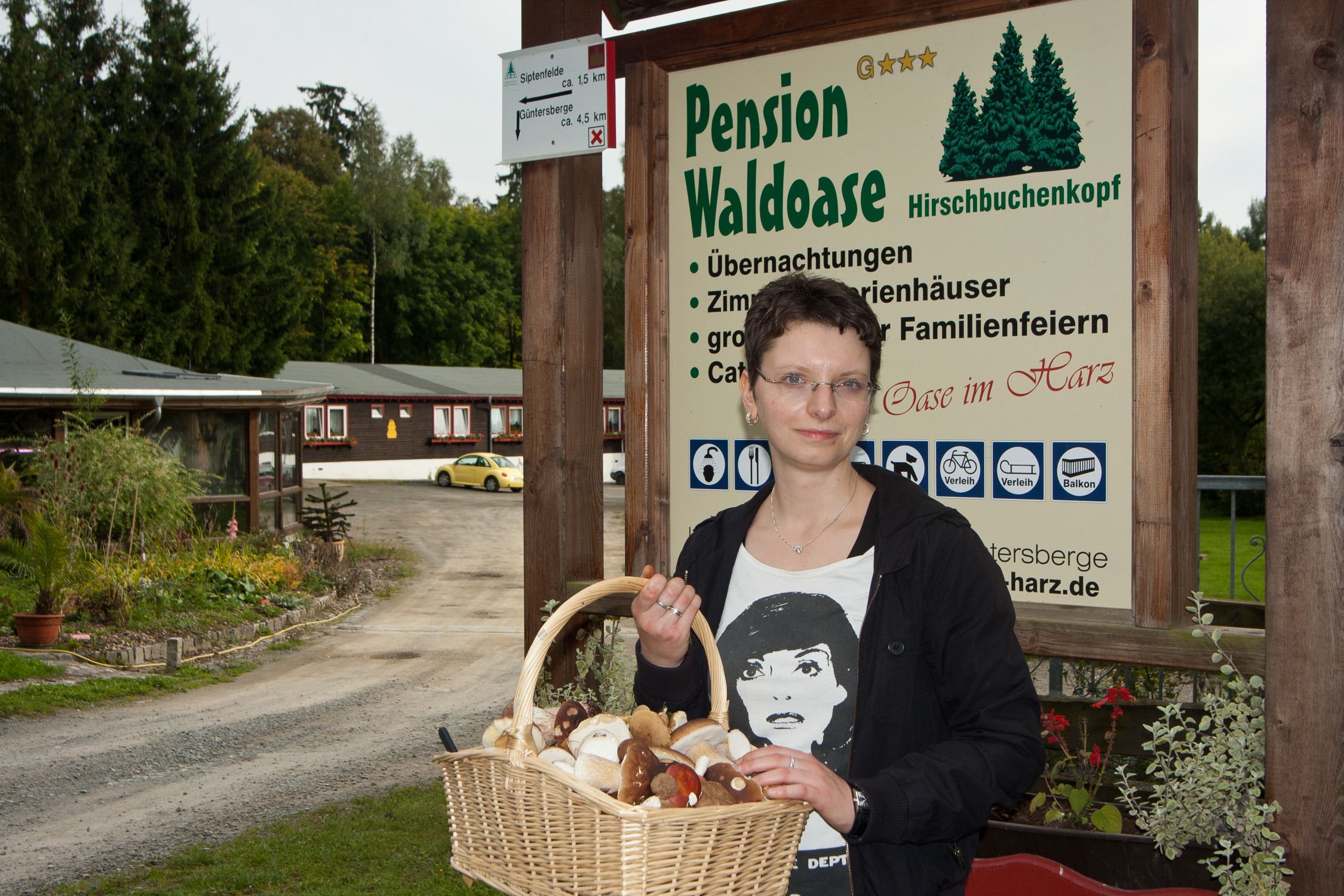 A woman holding a basket of food items in front of a sign for Pension Waldoase.