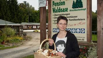 A woman holding a basket of food items in front of a sign for Pension Waldoase.