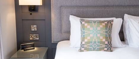 A neatly made bed with a patterned pillow, a bedside lamp, and a nightstand with a small electronic device.