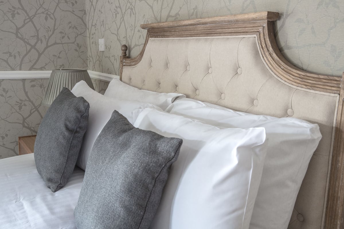 Un lit doté d’une tête de lit capitonnée, de coussins blancs et gris et d’un cadre en bois.