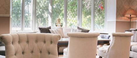 Un salón amplio con ventanas grandes, un sillón capitonado, un sofá y una lámpara.