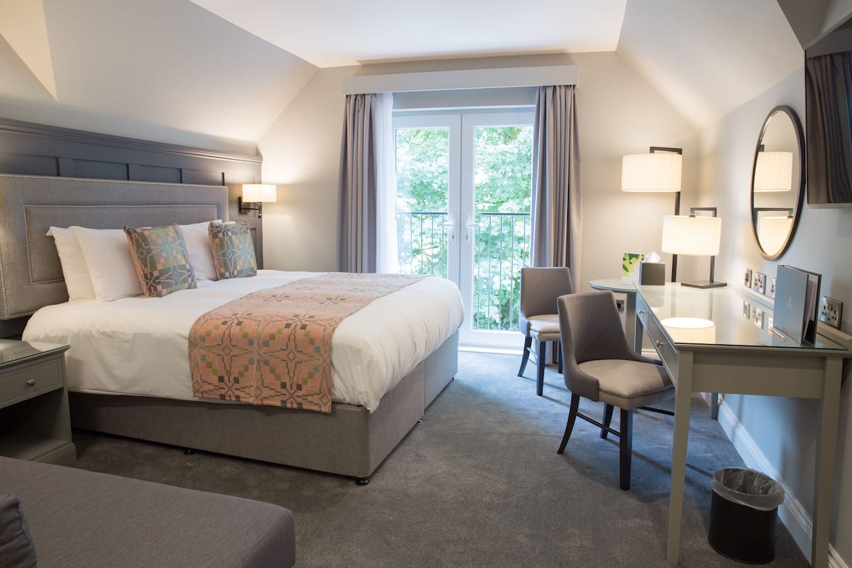 Une chambre d’hôtel avec un grand lit, un bureau, une chaise, une poubelle et une vue sur l’extérieur.