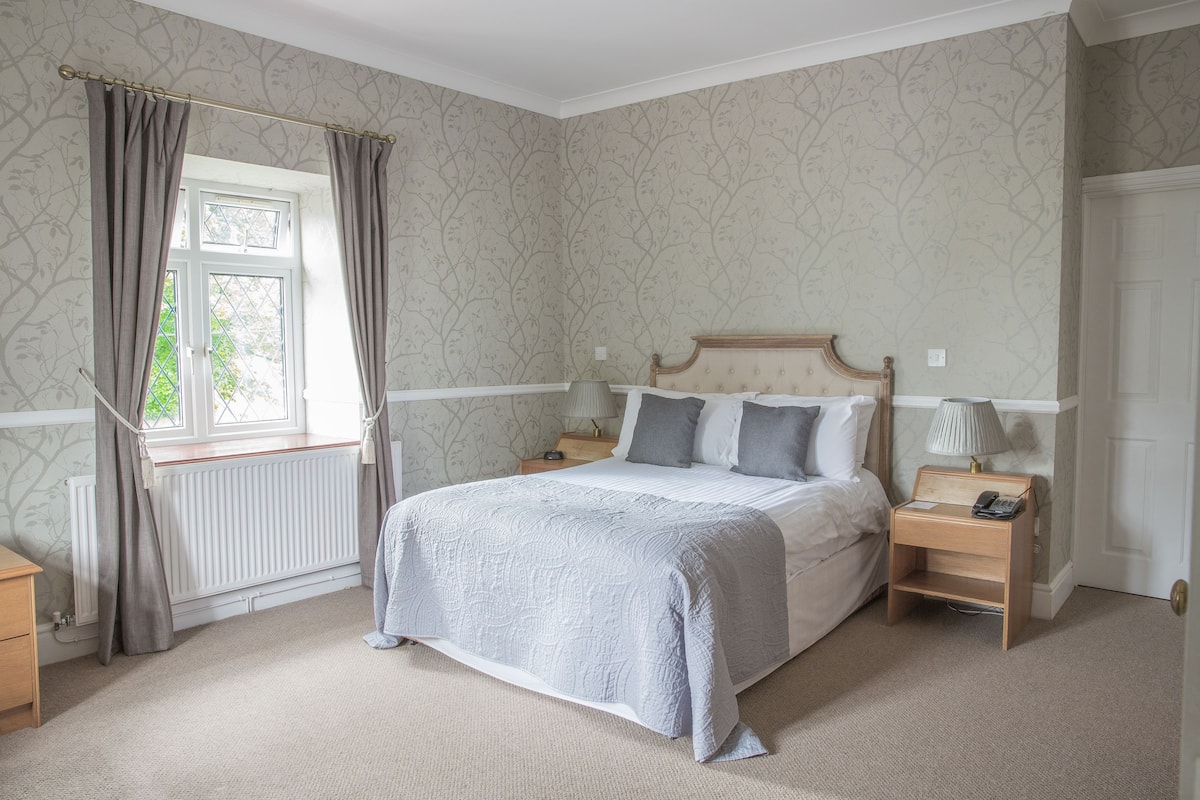 Une chambre à coucher avec un lit, des tables de chevet, une fenêtre avec des rideaux et un radiateur.