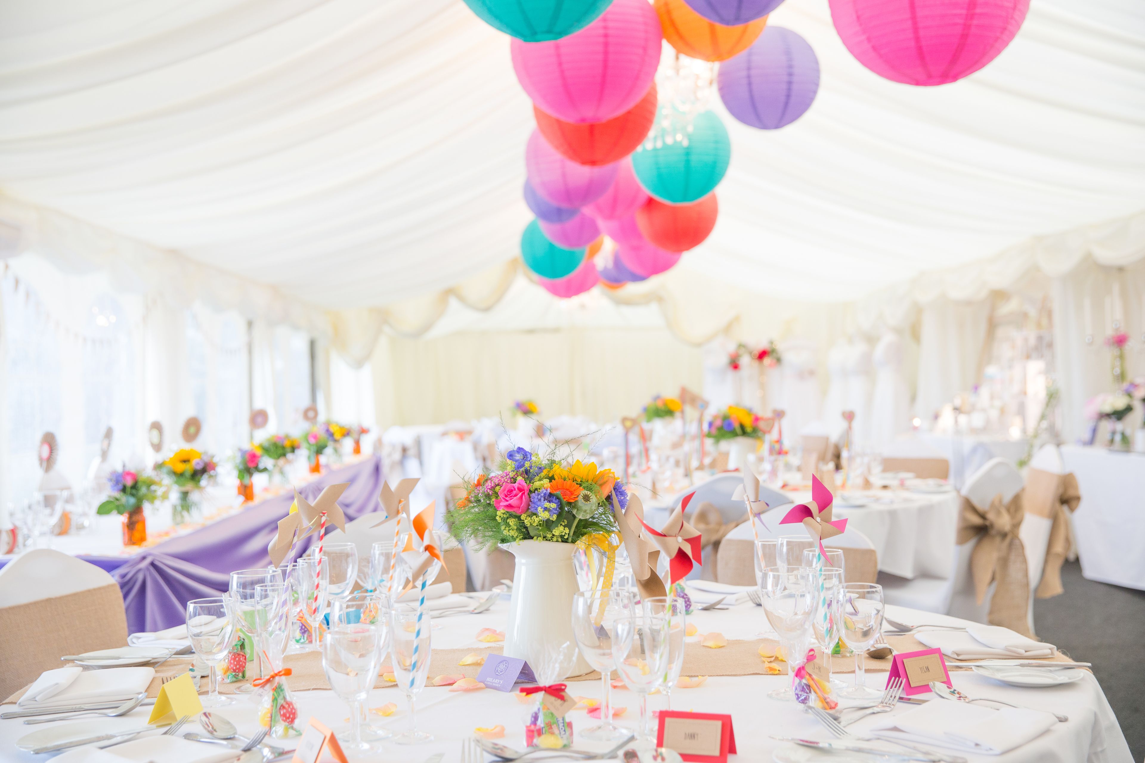 Uma sala de banquetes com mesas redondas preparadas para um evento formal, decorada com lanternas de papel coloridas e arranjos florais.