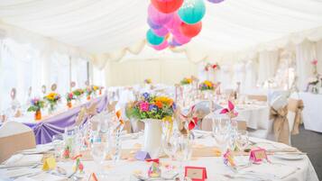 Uma sala de banquetes com mesas redondas preparadas para um evento formal, decorada com lanternas de papel coloridas e arranjos florais.